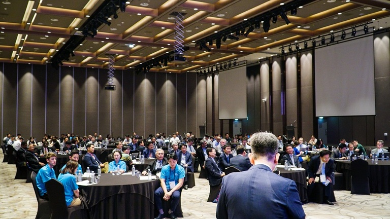 dozens of people sitting at round tables in a large room